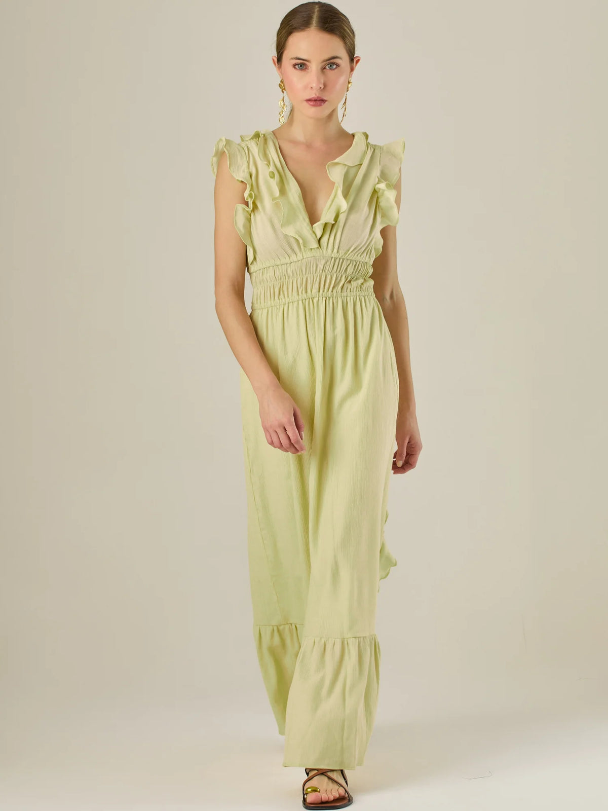Vestido largo sin mangas con escote en "V" profundo y un diseño con volantes que recorren tanto los tirantes como la parte frontal del busto y la falda. La cintura está fruncida con elástico para dar definición y comodidad, mientras que la falda fluye suavemente con un detalle de volante en el dobladillo, aportando movimiento y un aire femenino al conjunto.