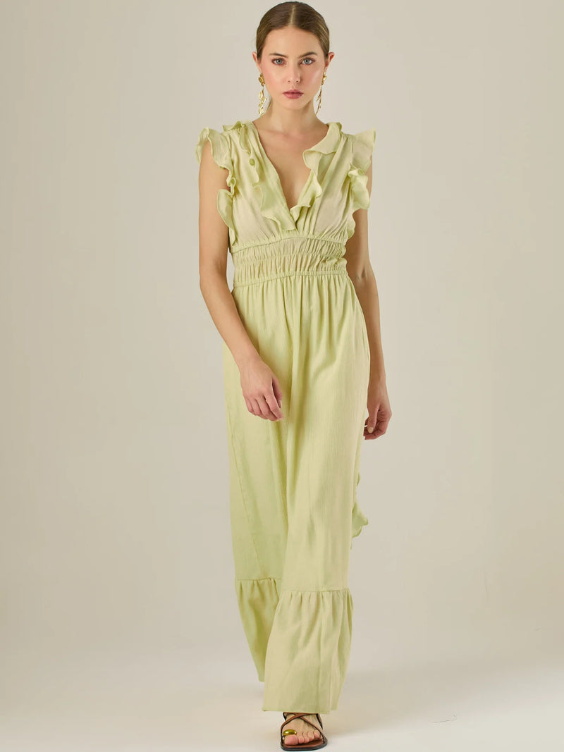 Vestido largo sin mangas con escote en "V" profundo y un diseño con volantes que recorren tanto los tirantes como la parte frontal del busto y la falda. La cintura está fruncida con elástico para dar definición y comodidad, mientras que la falda fluye suavemente con un detalle de volante en el dobladillo, aportando movimiento y un aire femenino al conjunto.