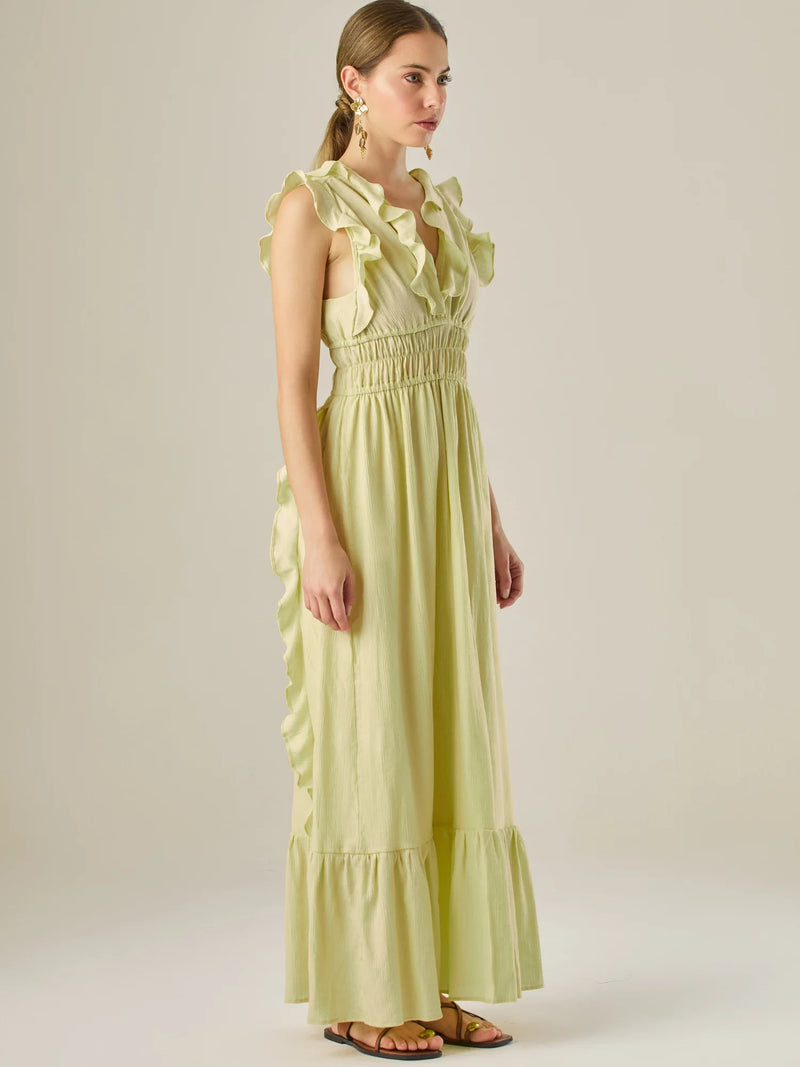 Vestido largo sin mangas con escote en "V" profundo y un diseño con volantes que recorren tanto los tirantes como la parte frontal del busto y la falda. La cintura está fruncida con elástico para dar definición y comodidad, mientras que la falda fluye suavemente con un detalle de volante en el dobladillo, aportando movimiento y un aire femenino al conjunto.